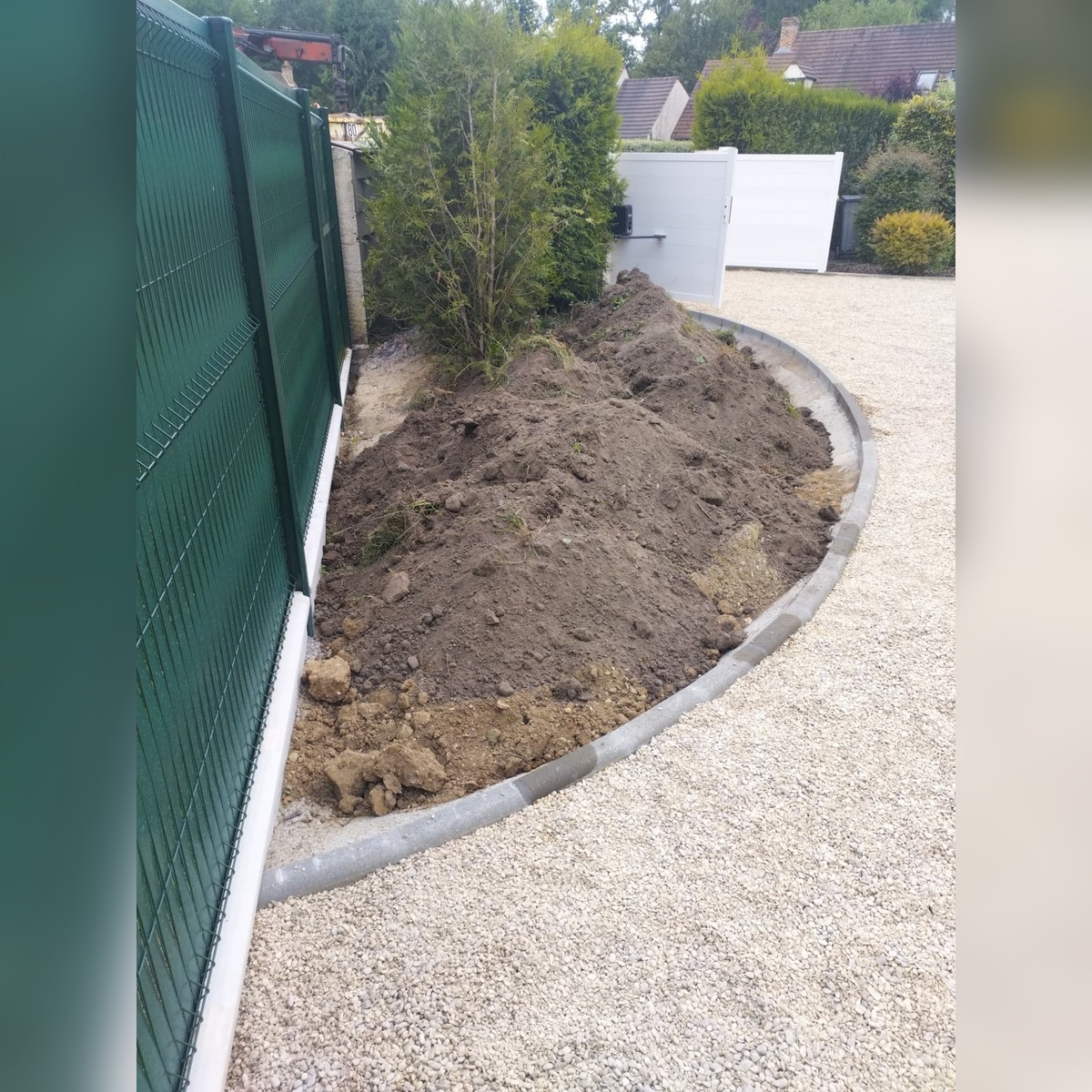 Terrassement en limite de propriété avec bordures béton, allée gravillonnée et clôture rigide
